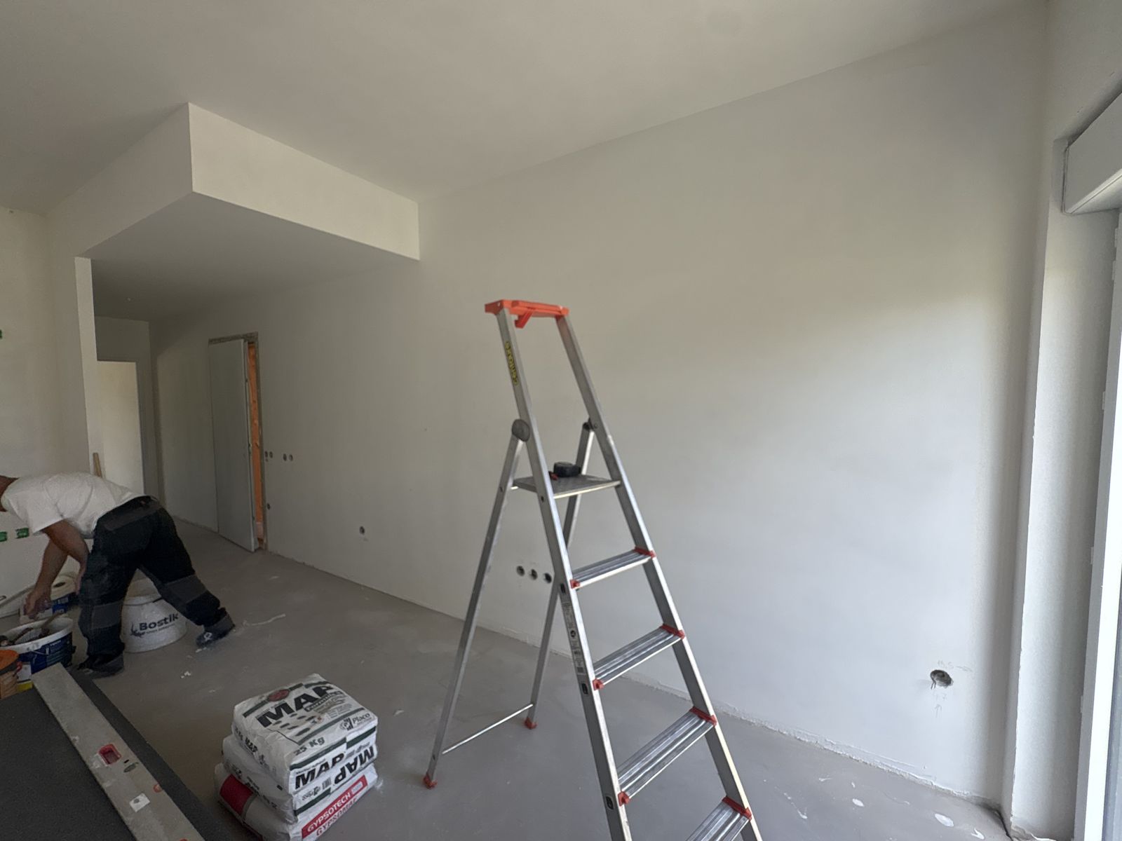 Intervenant préparant un logement neuf : échelle, enduit et reprises en cours
